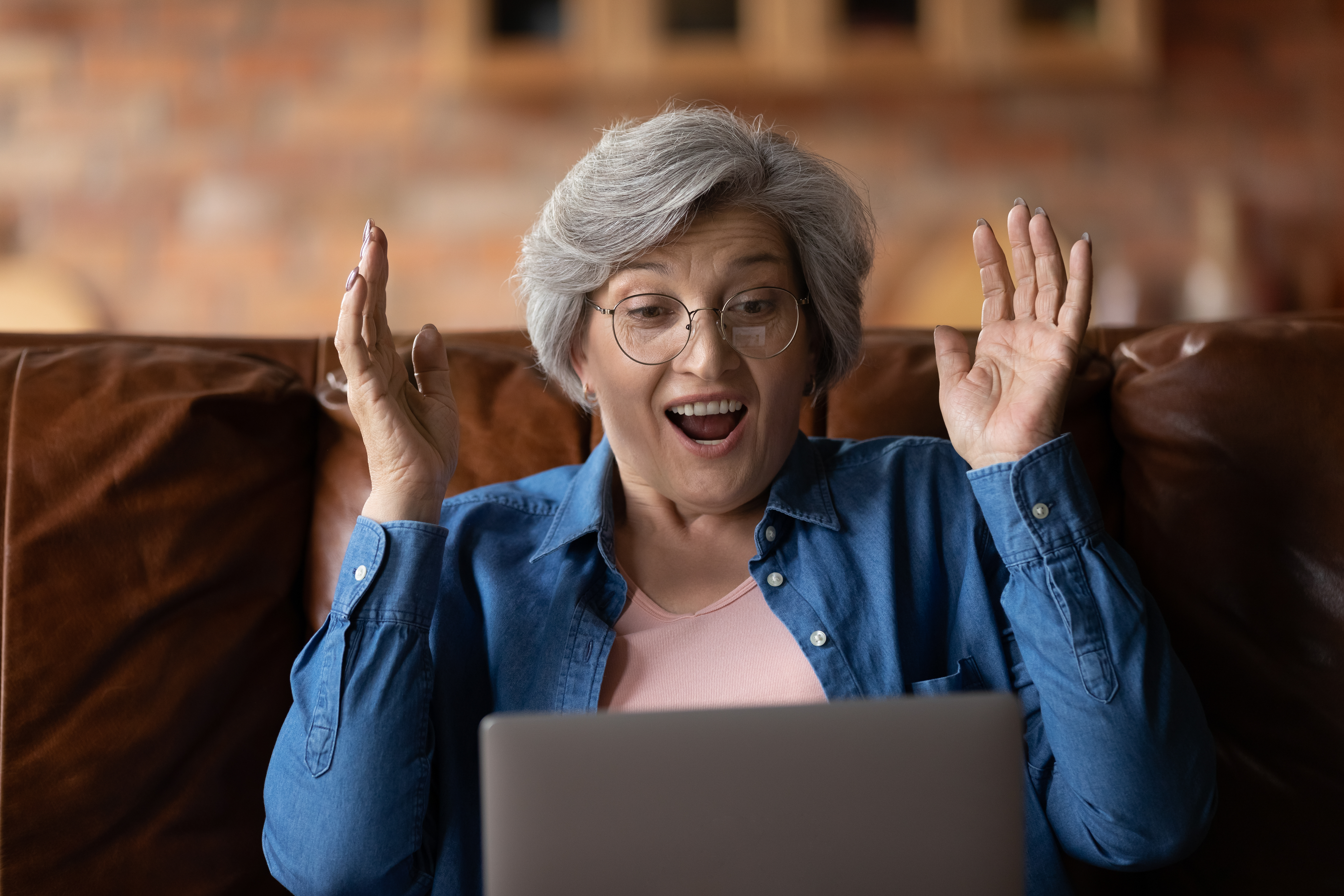 Mature woman with open mouth reading incredible news on laptop